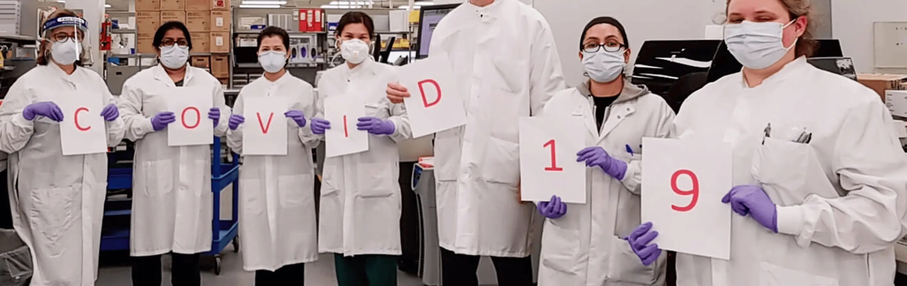 Group of Quest Diagnostic Techs holding signs with letters that spell out 'Covid-19'